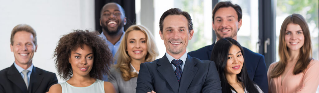 A group of people stand in front of a modern office building. The people are all wearing professional attire and appear to be smiling and engaged in conversation. The image conveys a sense of professionalism, teamwork, and engagement.